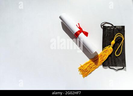 Pampille jaune de la casquette de graduation, rouleau de papier attaché avec ruban rouge avec noeud, diplôme et masque protecteur noir sur fond blanc, nouvelle réalité Banque D'Images