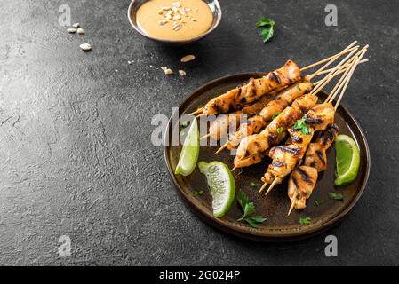 Brochettes de poulet grillé au satay servies avec de la sauce à la chaux et aux arachides sur un espace de copie noir. Cuisine asiatique de style thaïlandais. Banque D'Images