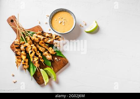 Brochettes de poulet grillé au satay servies avec de la sauce à la chaux et aux arachides sur fond blanc, espace de photocopie. Cuisine asiatique de style thaïlandais. Banque D'Images
