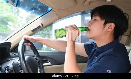 Un jeune homme asiatique boit de la bière tout en conduisant une voiture. Conduire sous l'influence. Banque D'Images