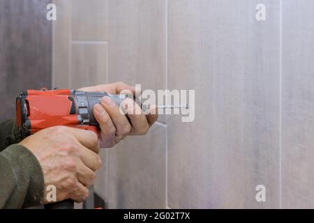 Mains de plombier à l'aide d'une perceuse pour créer de nouveaux trous salle de bains carrelée Banque D'Images