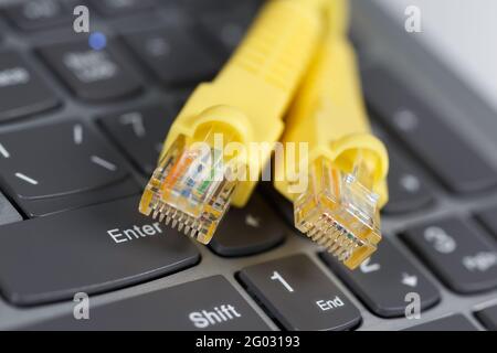 Deux connecteurs RJ-45 avec un fil jaune se trouvent sur le clavier de l'ordinateur portable. Banque D'Images