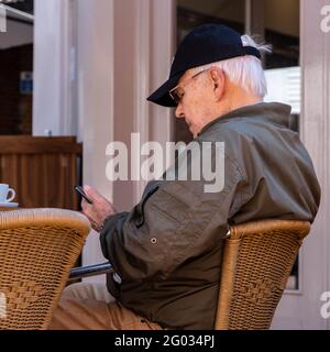 Epsom Surrey Londres, le 31 2021 mai, homme âgé assis seul dans UN restaurant ou un café en terrasse utilisant UN téléphone portable et ayant UN café Banque D'Images