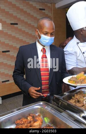 KAMPALA, OUGANDA - 27 mai 2021 : un homme bien habillé dans une suite se nourrissent et à côté du chef portant des vêtements blancs a son masque sur le visage Banque D'Images