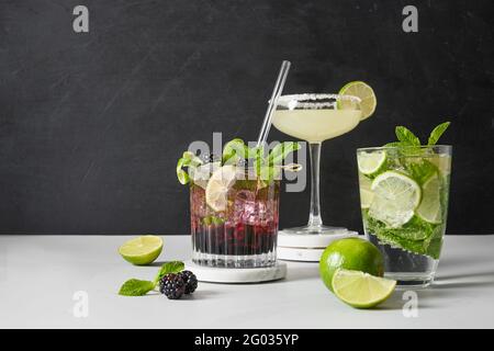 Cocktails mojito classiques et mûres avec citron vert sur fond noir et blanc dans un style moderne. Trois boissons d'été pour les fêtes. Su Banque D'Images