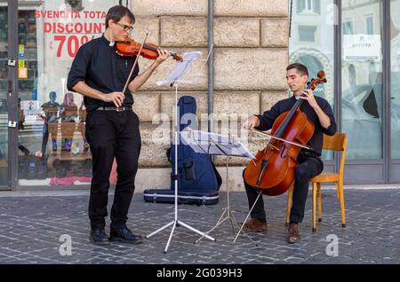 Deux jeunes prêtres catholiques jouent du violon et du violoncelle dans le rue Banque D'Images