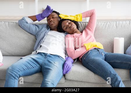 Homme et femme afro-américains fatigués se reposant après le nettoyage de l'appartement Banque D'Images