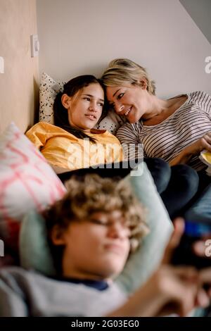 Mère souriante regardant sa fille en étant couché sur le lit à la maison Banque D'Images