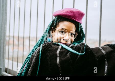 Portrait d'une femme adulte de taille moyenne souriante avec cheveux tressés bleus portant une béret par clôture Banque D'Images
