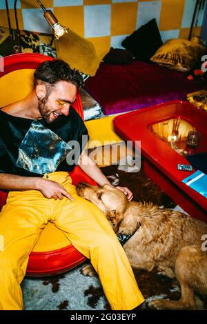 Jeune homme souriant assis avec un chien dans la salle de séjour Banque D'Images