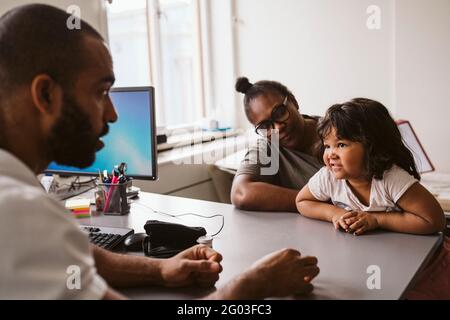 Pédiatre masculin parlant à une fille assise avec sa mère à son bureau Banque D'Images
