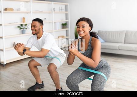 Jeune tenue noir couple entraînement avec élastique de résistance élastique en caoutchouc, faisant des squats à la maison Banque D'Images