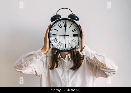 Jeune femme d'affaires couvrant son visage avec une horloge analogique vintage Banque D'Images