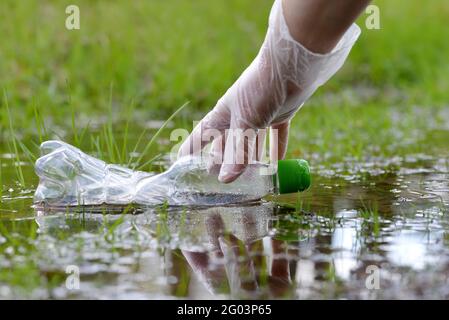 Une femme saisit à la main une bouteille en plastique de la flaque d'eau de la forêt. Concept de conservation de la nature. Banque D'Images