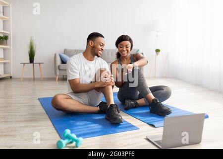 Un jeune couple noir prend une pause après un entraînement à domicile, regardant un didacticiel vidéo sur un PC portable, à l'intérieur Banque D'Images