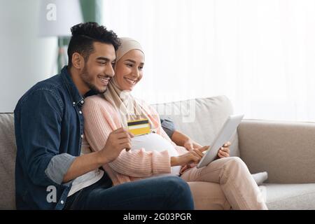 Joyeux couple musulman enceinte magasiner en ligne, en utilisant une carte de crédit et une tablette numérique Banque D'Images