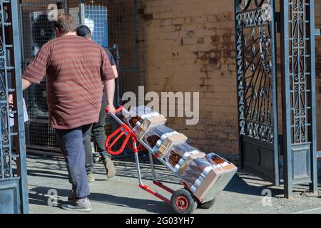 Un homme adulte livre une boisson sur un chariot. Un employé tire un chariot à boissons pliable. Banque D'Images