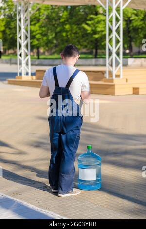 Un homme adulte en combinaison livre de l'eau potable aux magasins. Un travailleur se tient avec un baril d'eau potable. Banque D'Images