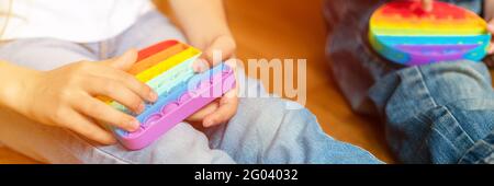 anti stress sensory pop it jouets dans les mains d'un enfant. un petit enfant heureux joue avec un simple jouet à fossettes à la maison. les tout-petits tiennent et jouent popit Banque D'Images