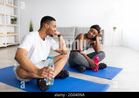 Un gars noir funky et sa petite amie qui prennent une pause après l'entraînement domestique, tenant des bouteilles d'eau, restant hydraté à la maison Banque D'Images