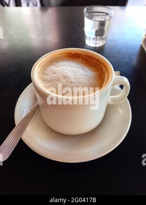 une tasse de lait mousseux et de café pour le petit déjeuner sur fond de table noire dans un café Banque D'Images