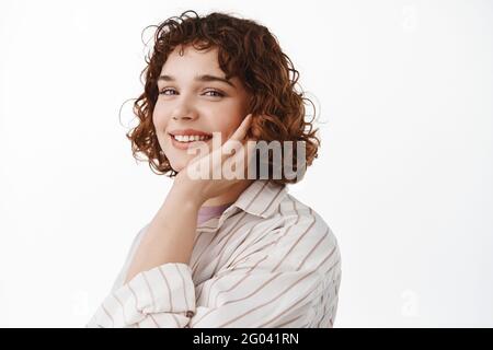 Soins de la peau et beauté. Jeune femme sans maquillage, touchant la peau fraîche et propre du visage, tenez la main sur la joue et souriez heureux à l'appareil photo, debout Banque D'Images