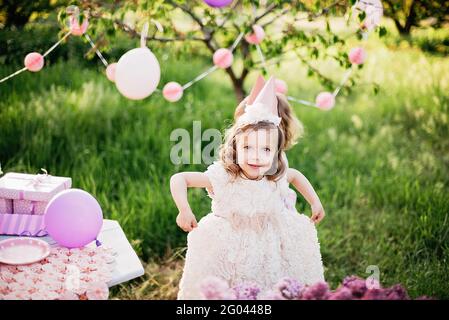 Joyeux anniversaire petite fille dans beau jardin. anniversaire de 4 ans. les enfants mangent un gâteau rose joyeux anniversaire. décoration colorée pastel à l'extérieur Banque D'Images