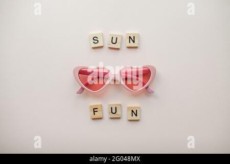Mise en page. Verres roses sous forme de coeurs sur fond rose clair. Inscription de blocs de bois Sun Fun Banque D'Images
