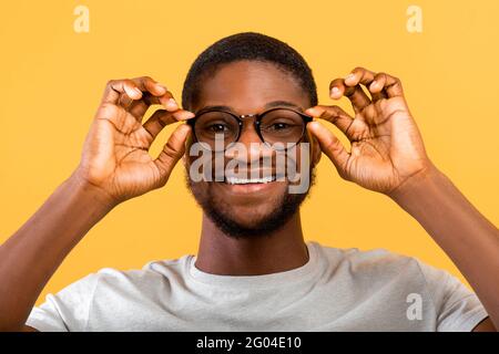 Positif afro-américain gars portant des lunettes, regardant et souriant à l'appareil photo sur fond jaune studio Banque D'Images