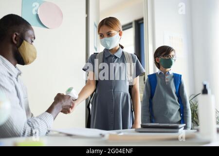 Portrait d'un enseignant de sexe masculin vérifiant la température des enfants entrant dans la classe à l'école, mesures de sécurité de la cavique Banque D'Images