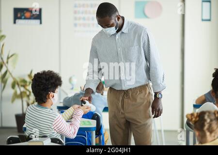 Portrait d'un professeur afro-américain assainisseur les mains des enfants en classe scolaire, mesures de sécurité des enfants, espace de copie Banque D'Images