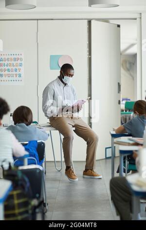 Portrait complet d'un enseignant afro-américain portant un masque dans une classe scolaire, mesures de sécurité de la cavique Banque D'Images