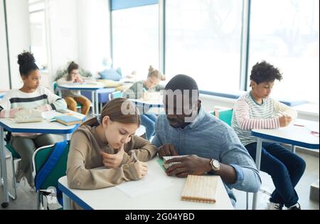 Portrait grand angle de l'enseignant masculin attentionné aidant la jeune fille dans la classe scolaire, espace de copie Banque D'Images