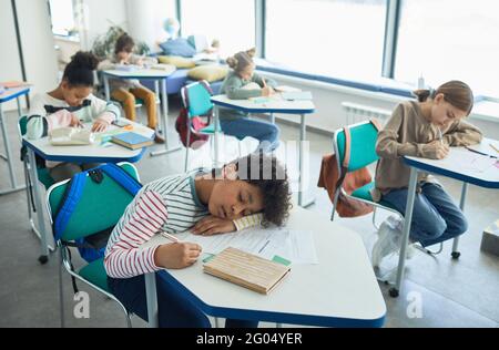 Portrait en grand angle d'un garçon à course mixte dormant au bureau dans une salle de classe scolaire, espace de copie Banque D'Images