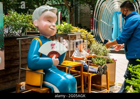 Un père fait poser son fils sur une chaise à côté d'une statue devant un restaurant autour de Xintiandi à Shanghai, en Chine. Banque D'Images