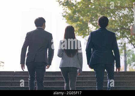 vue arrière de trois jeunes hommes d'affaires asiatiques prospères qui montent étapes Banque D'Images