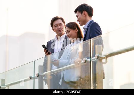 trois heureux hommes d'affaires asiatiques regardant le téléphone portable bavardant discuter pour les affaires en extérieur Banque D'Images