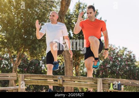 Instructeur de sport et un homme avec des vêtements de sport faisant des pas sur un banc de parc Banque D'Images