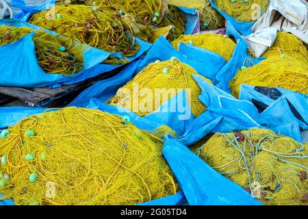 Filets de pêche séchant sous le soleil dans le port de pêcheur. Les filets de pêche de couleur jaune s'empilent sur le fond bleu des sacs. Matériel de pêche Banque D'Images