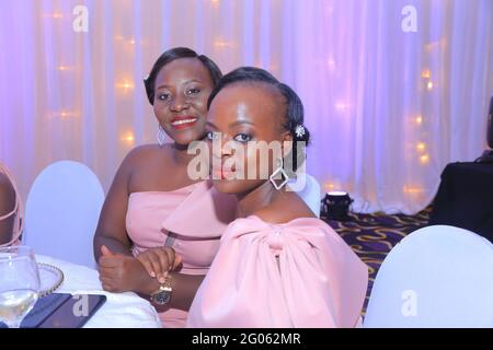 KAMPALA, OUGANDA - 31 mai 2021 : deux femmes de mariée noires afro-américaines à la table haute, prenant un verre le jour du mariage avec d'énormes sourires partout Banque D'Images