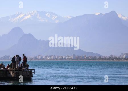 Antalya, Turquie décembre 22 2018: Silhouettes de pêcheurs contre la rive de la mer Méditerranée de la Turquie d'Antalya, taureau montagnes avec des sommets enneigés. Banque D'Images