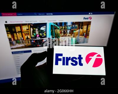 Personne tenant un téléphone portable avec le logo de la société britannique de transport FirstGroup plc sur l'écran devant le site Web d'affaires. Mise au point sur l'affichage du téléphone. Banque D'Images