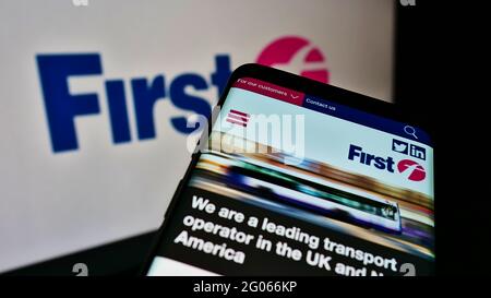 Téléphone mobile avec le site Web de la société de transport britannique FirstGroup plc à l'écran devant le logo de l'entreprise. Faites la mise au point dans le coin supérieur gauche de l'écran du téléphone. Banque D'Images