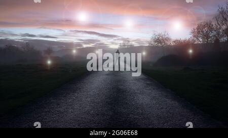 Un concept OVNI d'orbes lumineux, flottant au-dessus d'une route d'hivers brumeux juste après le coucher du soleil. Avec une silhouette détourée , de retour à la caméra, en regardant la lumière Banque D'Images