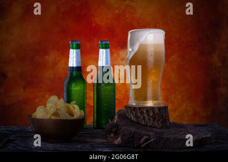 Verre de bière fraîche pinte avec mousse à côté de deux bouteilles vertes de bière lager. Bouteilles et verre avec gouttes d'eau. Banque D'Images