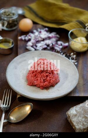 Ingrédients pour la préparation du tartare de boeuf sur un vieux panneau de découpe en bois, tissu de cuisine et fond en métal rouillé, Italie, Europe Banque D'Images