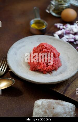 Ingrédients pour la préparation du tartare de boeuf sur un vieux panneau de découpe en bois, tissu de cuisine et fond en métal rouillé, Italie, Europe Banque D'Images