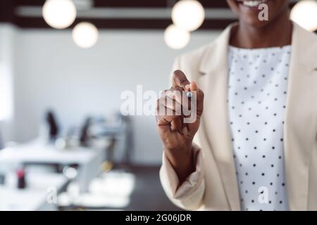 Gros plan de la main d'une femme d'affaires afro-américaine écrivant sur un écran interactif Banque D'Images