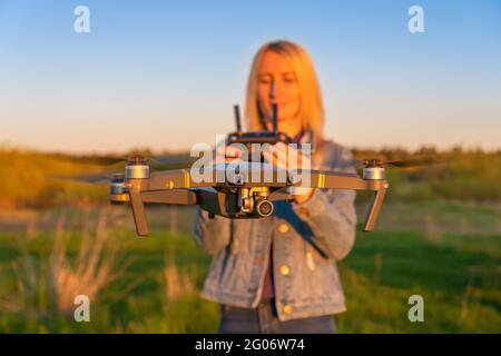 Une jeune femme blonde contrôle un drone dans la nature pendant le coucher du soleil. Au premier plan se trouve un drone de gros plan Banque D'Images