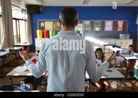 Vue arrière de l'enseignement masculin de race blanche à divers élèves de la classe à l'école élémentaire Banque D'Images